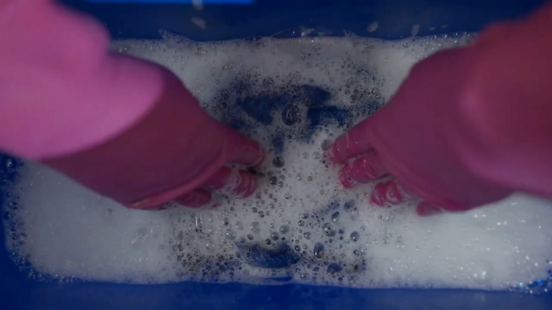 Hands Wearing Pink Gloves Are Scrubbing Clothes in A Soapy Water Solution, Likely for Removing Diesel Smell