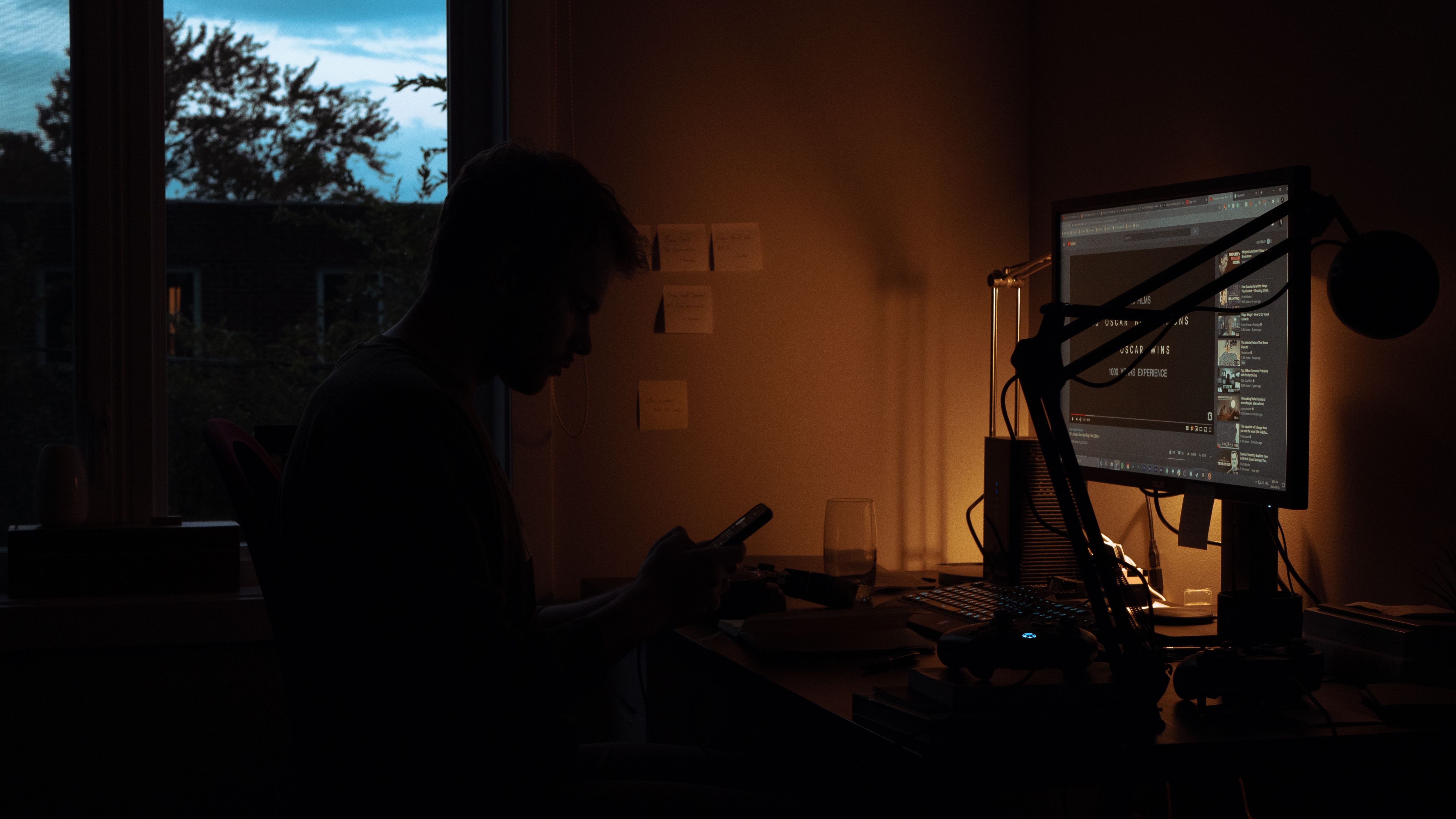 Silhouette of a person using a smartphone in a dark room, symbolizing screen-driven connection and isolation